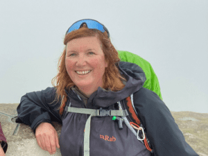 Image shows a woman Nicky Button who is the walk leader. Nicky is in walking gear and is wearing the type of big smile that you only get from enjoying the great outdoors.