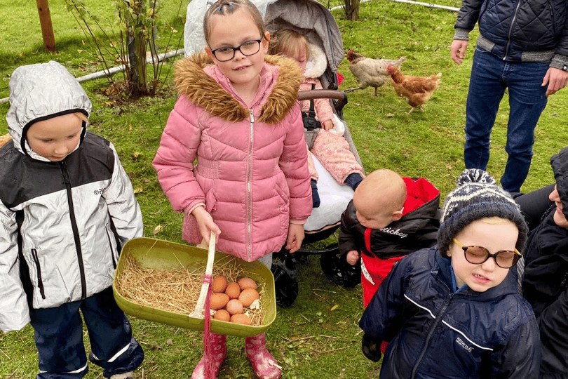 children in warm coats standing in a field, one is golding a basket of fruit